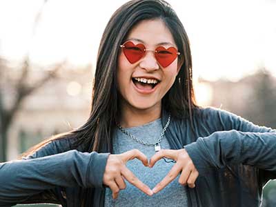 young woman making heart symbol with hands and smiling at camera