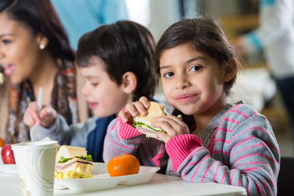 Young girl eating sandwich at school cafeteria lunch table