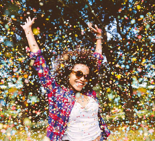 excited girl wearing sunglasses throwing arms up in celebration in a shower of confetti