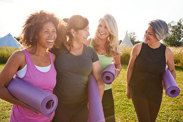 group of older ladies walking and talking, smiling, carrying yoga mats outdoors