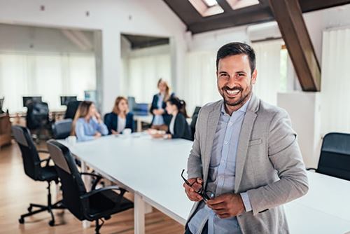 focus on a man smiling at the end of a table while a group of business people converse behind him