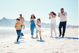 A multi-generational family following their young children as they run happily on the beach