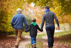 A grandfather and his adult son walking with the young grandson between them in the fall leaves