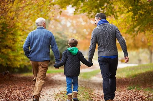 A grandfather and his adult son walking with the young grandson between them in the fall leaves