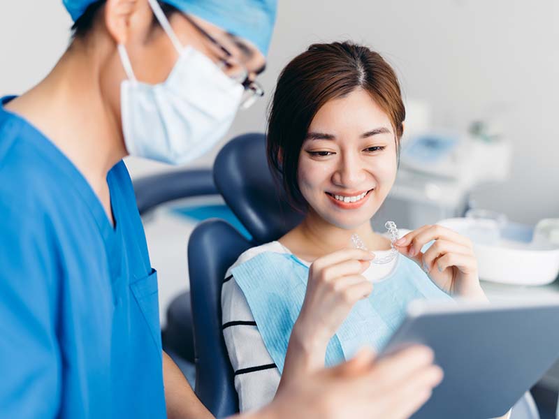 Asian dentist with Asian women patient holding a tablet in a dentist office.