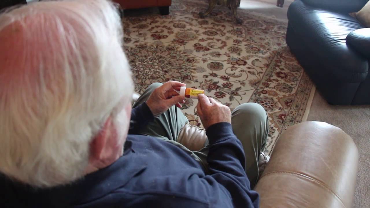 Man sitting in a chair taking medication from a bottle