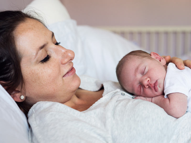 Mother in bed holding newborn baby. (halfpoint/envato elements)