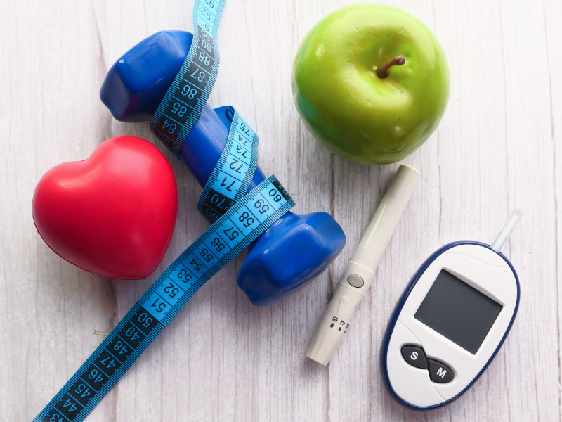 a collection of objects on a table: a hand weight wrapped with a tape measure, an apple, a heart-shaped stress ball, and weight measurement tools