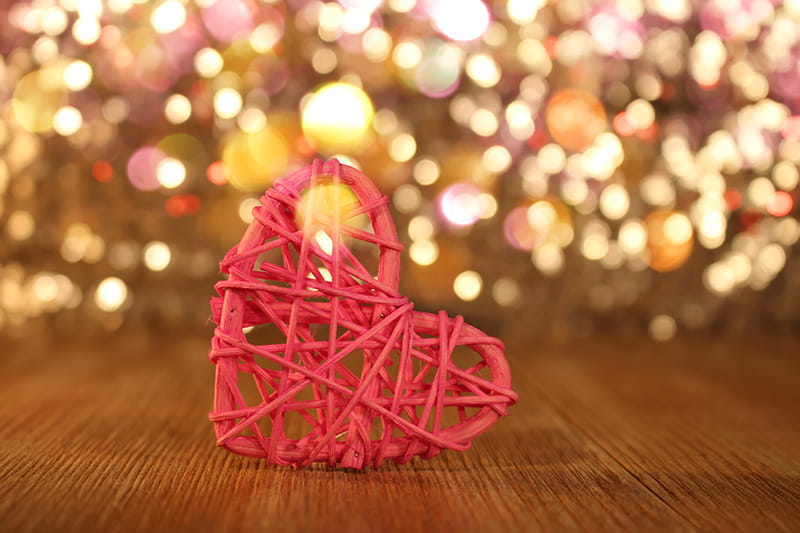 A woven heart in the foreground in front of a sparkly holiday backdrop