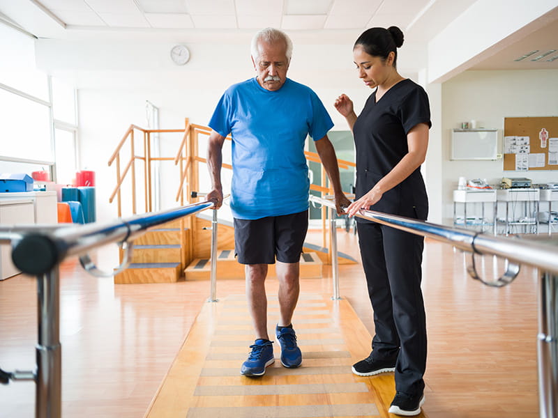 an older man practices walking with help from a healthcare worker in a rehab facility