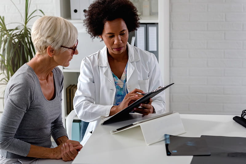 An older woman sitting with her doctor looking over information on a tablet