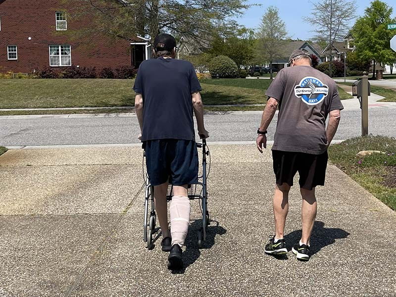 Kyle Hartley walking using a walker with his father, David, by his side