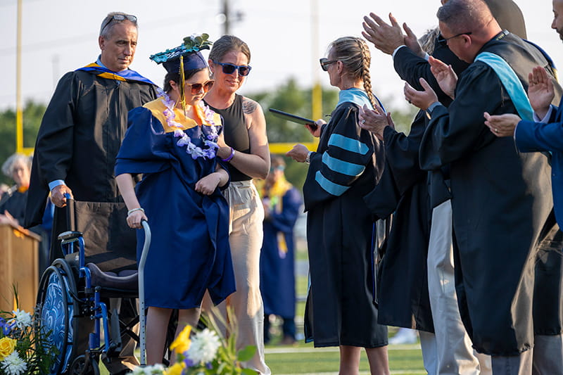 Bella Chambasis with her mom, Deann, at her side, standing up from her wheelchair to receive her high school diploma