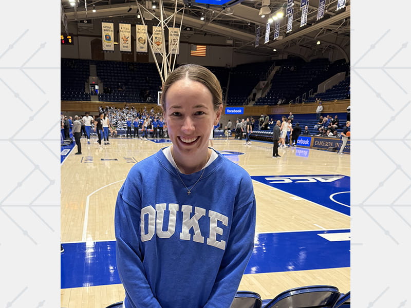 Dr. Michelle Kelsey wearing a Duke sweatshirt standing courtside at a Duke-Virginia basketball game at Cameron Indoor Stadium in NC