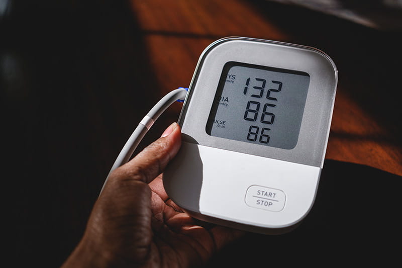 close-up of a hand holding a blood pressure monitor with numbers on the screen