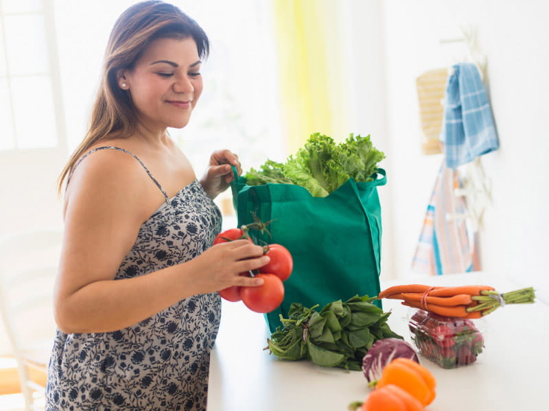 Woman unpacking fresh vegetables from a grocery bag.