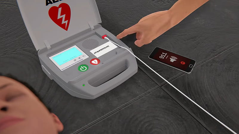an illustration of an AED with a hand reaching to press the buttons, video screenshot
