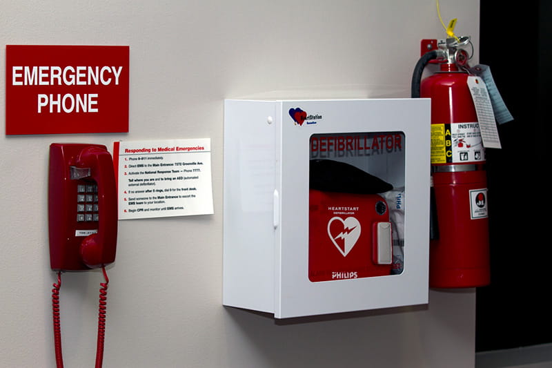 an AED stored on the wall next to a fire extinguisher and an emergency phone