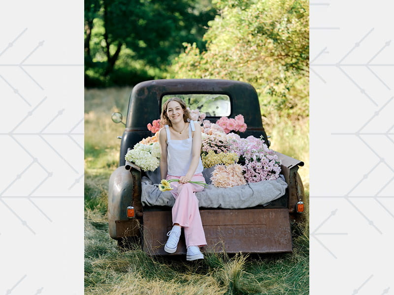 Caroline Laubach posing and smiling in the back of an antique truck filled with flowers