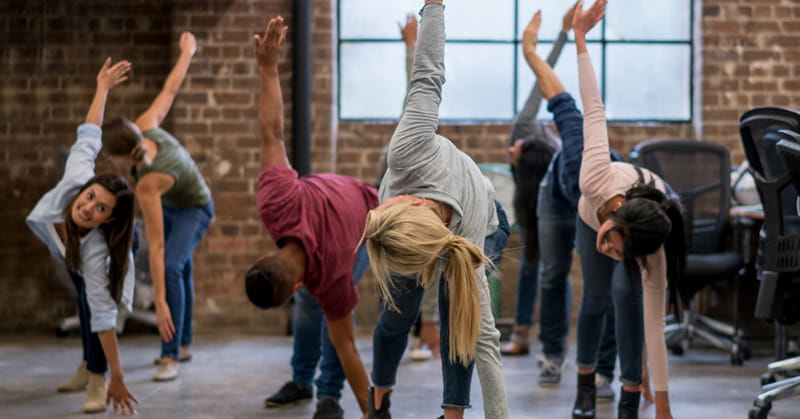 several young adult office workers taking a stretch break in an open space near their desks
