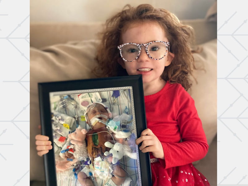 Congenital heart defect survivor Corey Jenness, now 6, holds a photo of herself as a newborn recovering from open-heart surgery. (Photo courtesy of the Jenness family)