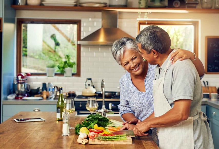 Older couple smiling, cutting vegetables together in kitchen