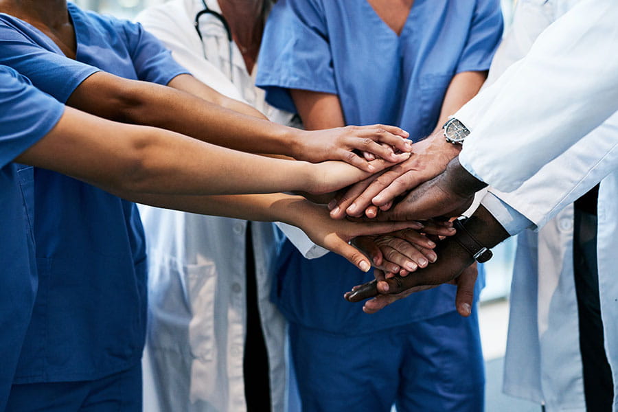 view of diverse healthcare workers from neck down, standing in circle hands all together in center