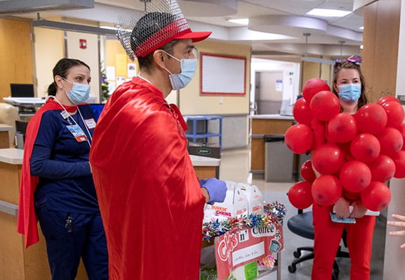 Three healthcare professionals dressed in red capes and blood clot costumes