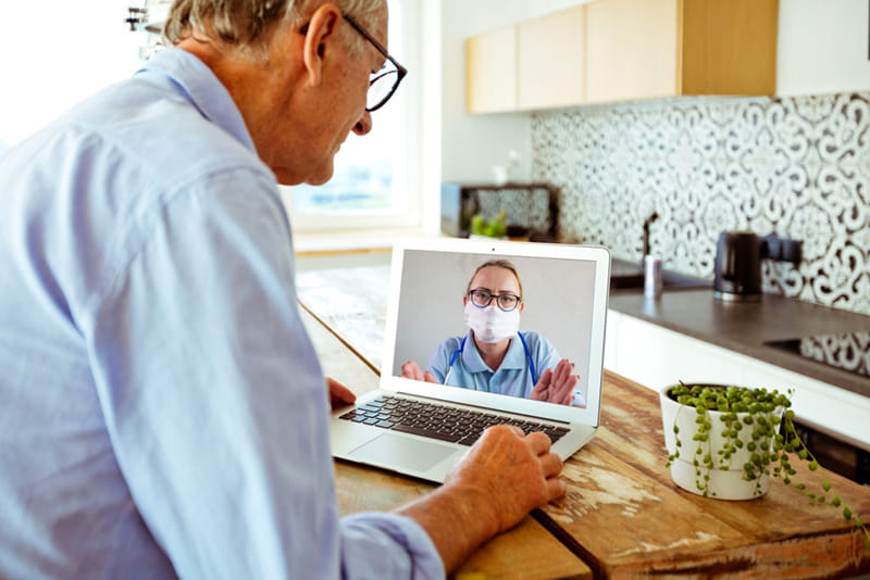 Elder man at home speaking to medical professional via video conference on laptop