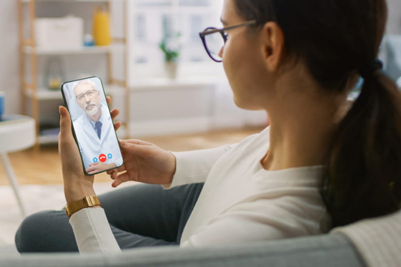 Woman at home on couch speaking to medical professional via video call on her phone