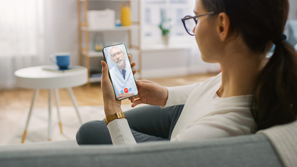 Woman sitting on couch at home using telehealth service on her phone