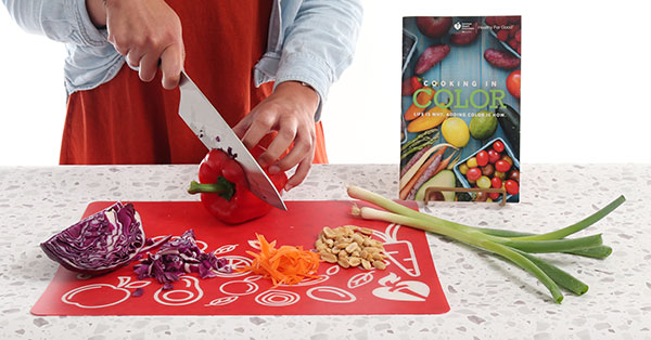 Cloe up of hands chopping vegetables on cutting board with American Heart Association Cooking in Color cookbook