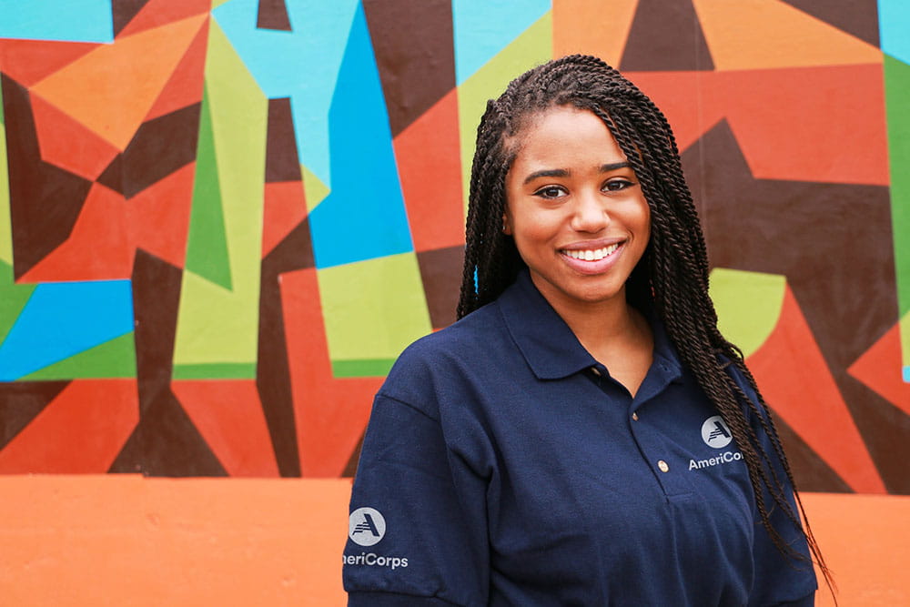 AmeriCorps smiling young woman volunteer posing in front of abstract mural