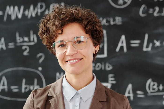 Club advisor, smiling, standing in front of chalkboard with equations written on it