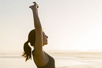A young woman stretching in the sunshine at the beach