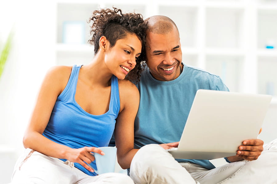 Young to middle age adult couple sitting on living room floor looking at laptop together