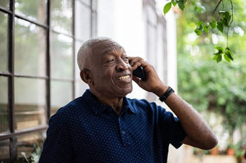 Older black man smiling talking on the phone outside