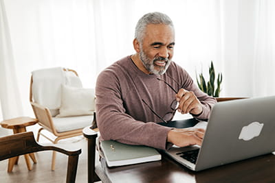 older man sitting at table at home working on a laptop