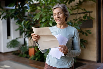 older woman standing outside at home reading a letter
