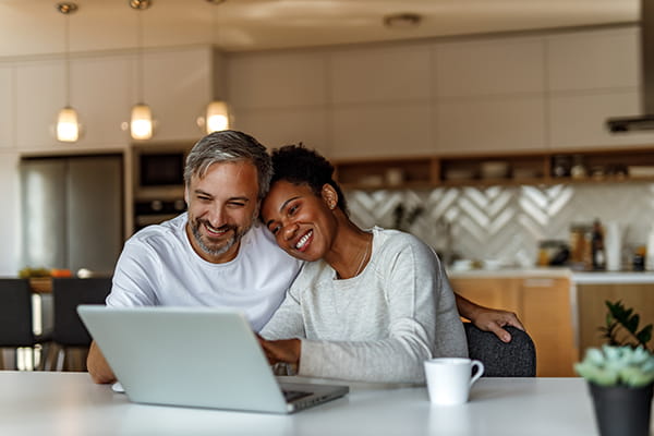 an older adult couple smiling, watching a laptop screen together in the kitchen