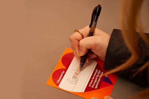 woman's hand writing a name on a heart-shaped donation paper