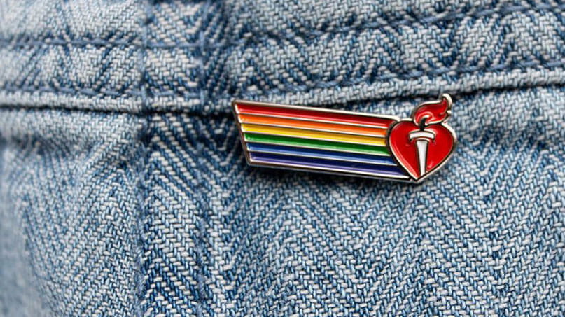 close-up of a blue denim jacket with a Pride with Heart logo pin on it