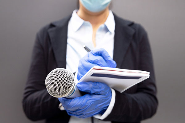 Masked reporter holding a microphone and taking notes