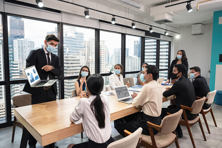 Businessman wearing face mask with presentation of business plan on laptop, corporate business meeting in modern office while pandemic of virus