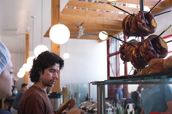 Two Firebrand participants are working behind the counter in a bakery and coffee shop.