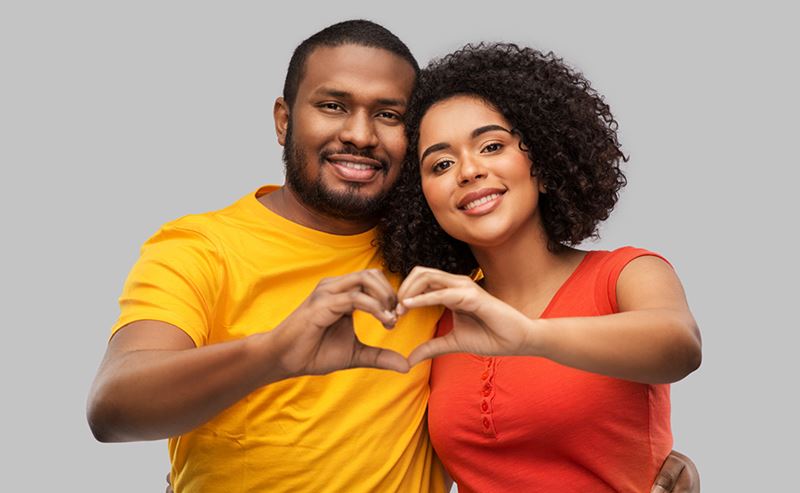 male and female smiling at camera while making heart with their hands