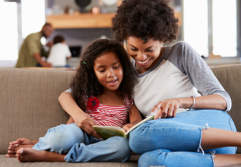 mother and daughter sitting on couch reading a book