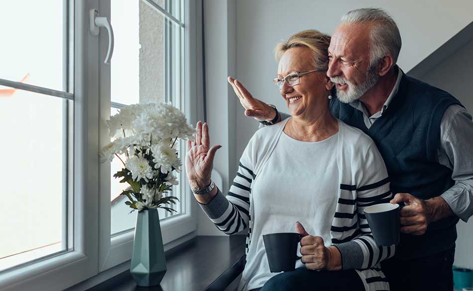husband and wife waving outside a window from inside of house