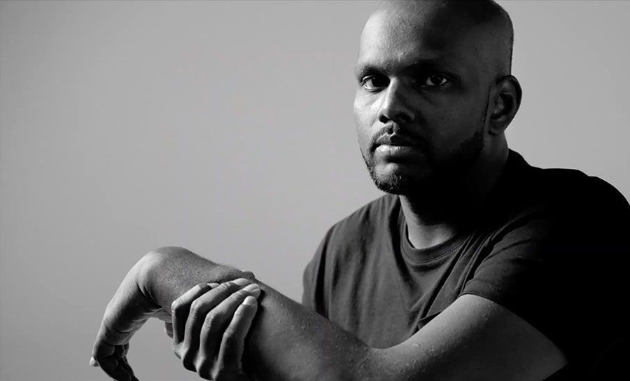 black and white image of african american man holding left arm and looking at camera