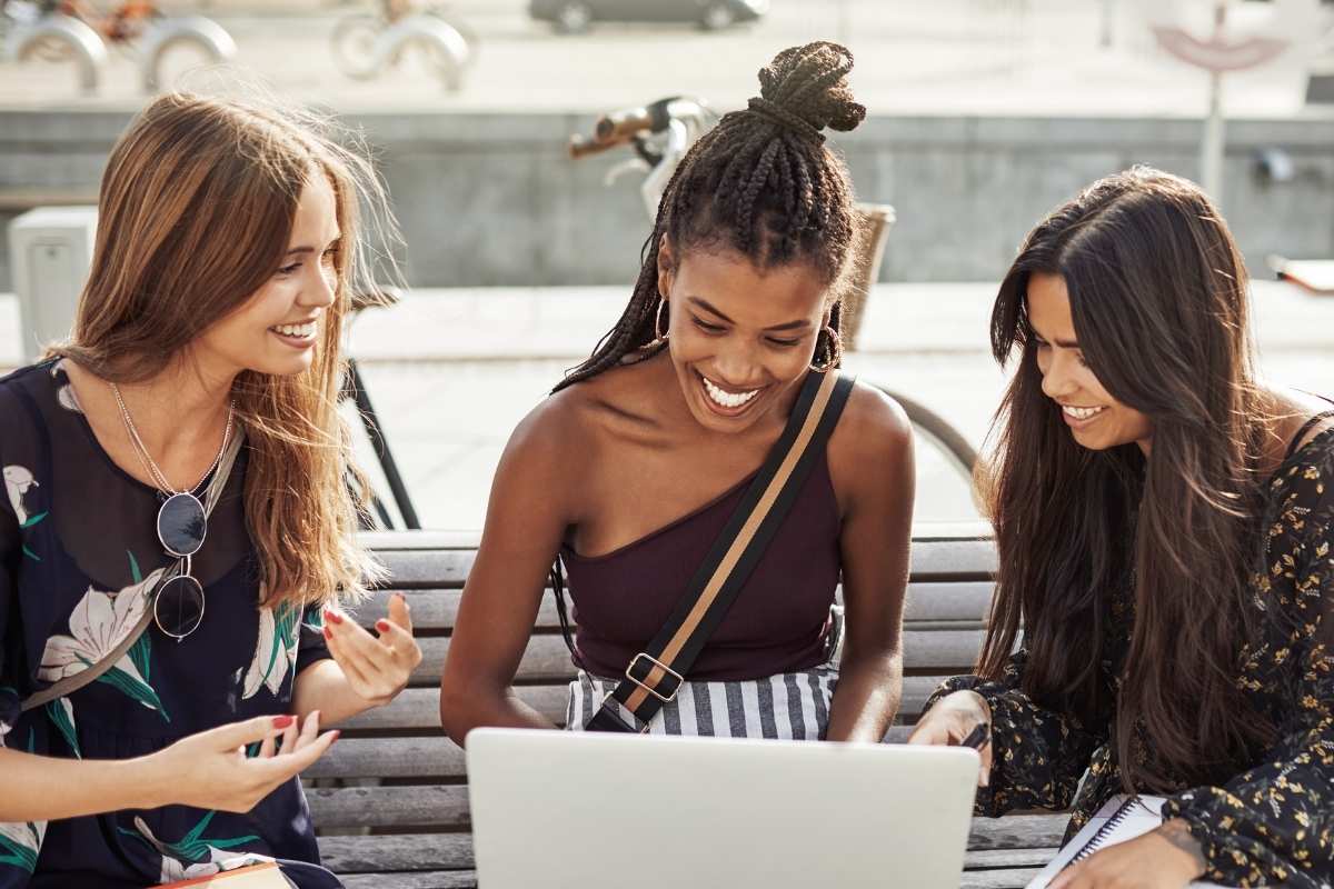 three young women seated around laptop